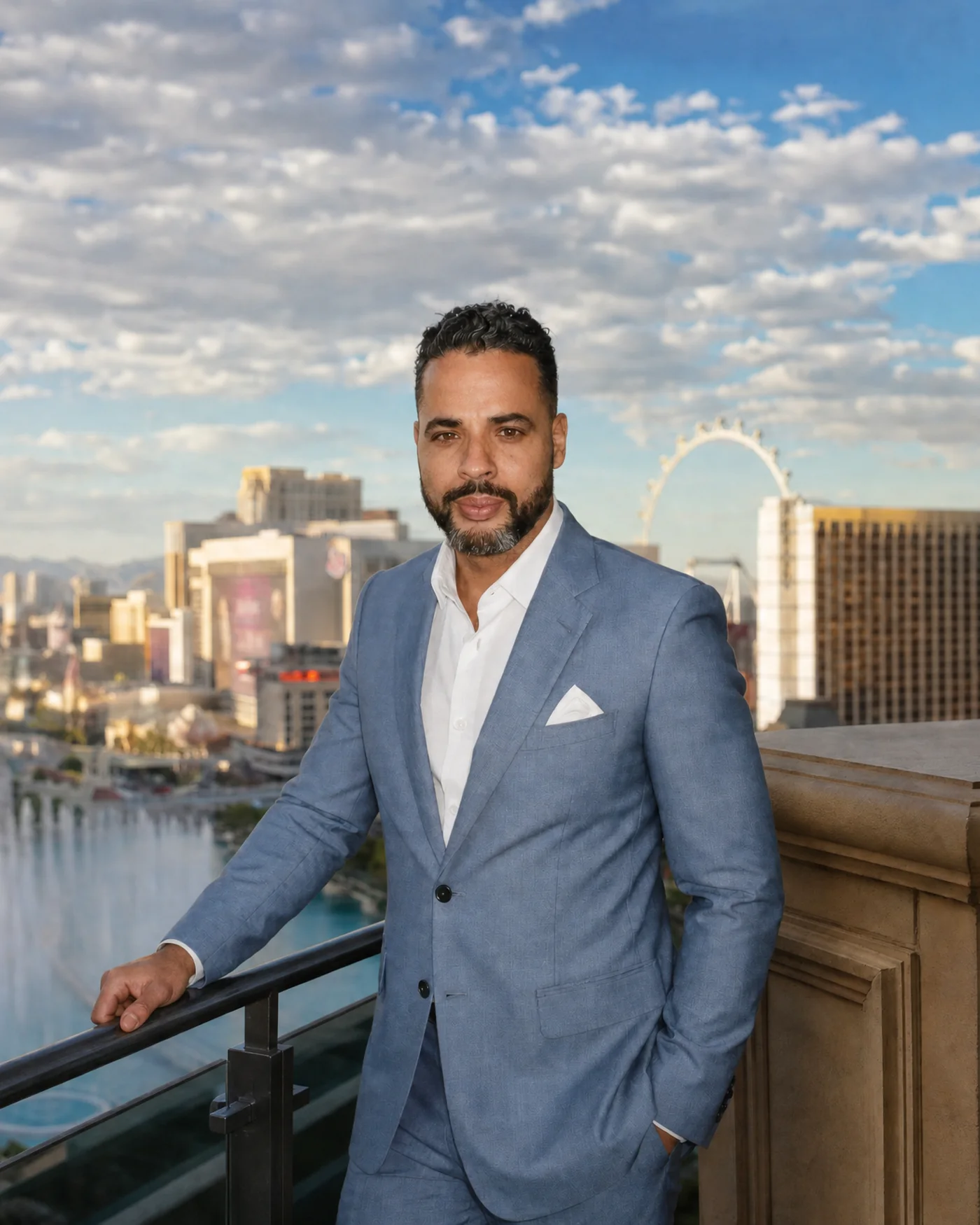 Nicholas Aponte-Rodriguez on a balcony above the Las Vegas Strip, the Bellagio fountains and the Paris tower behind him, in a light blue suit.